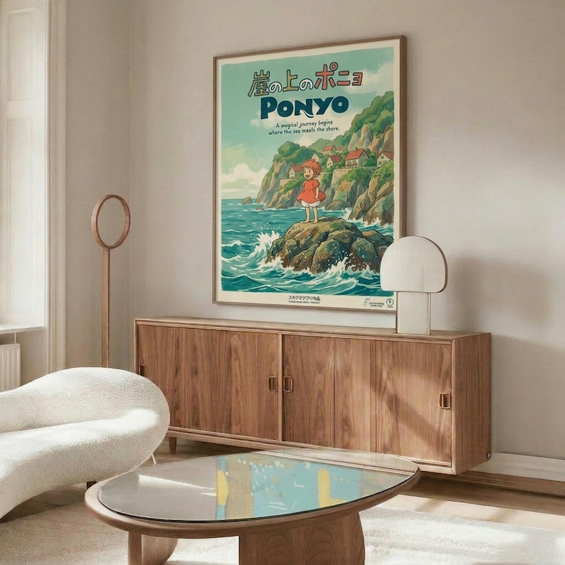 May include: Studio Ghibli Ponyo movie poster displayed in modern living room with warm wood credenza, white curved chair, and glass coffee table. Poster shows young girl in red dress standing on rocky coastline with green cliffs and turquoise ocean waves. Japanese text at top with "PONYO" in blue letters below. Minimalist room has cream walls, natural lighting, and mid-century furniture in walnut tones.