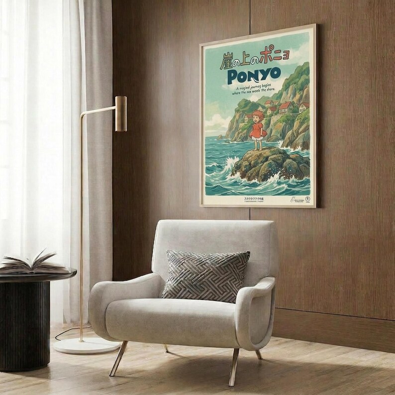 May include: Framed Ponyo poster on wood-paneled wall above cream upholstered armchair with geometric pillow. Poster shows red-dressed girl character on coastal cliffs with turquoise ocean waves, green hills, and Japanese text. Modern living room setting with brass floor lamp, dark side table with open book, and natural lighting from window with curtains.