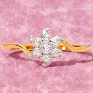 Könnte beinhalten: Ein goldener Ring mit einem zentralen, blumenförmigen Motiv aus silberfarbenem Metall. Das Blumendesign ist mit sieben kleinen, runden, klaren Steinen besetzt, einer in der Mitte und sechs drumherum, was ein funkelndes, symmetrisches Blumenmuster ergibt.