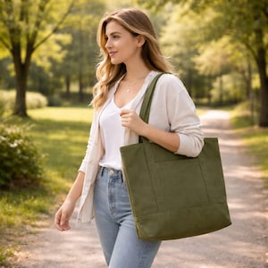 Może przedstawiać: Zielona płócienna torba typu tote w kształcie prostokąta z przednią kieszenią. Torba ma solidne uchwyty i jest noszona na ramieniu. Jest to praktyczny dodatek do codziennego użytku.