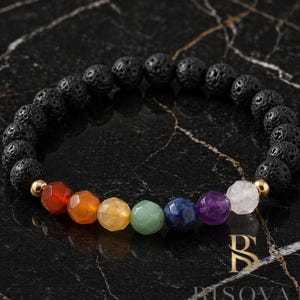 Peut inclure: Bracelet en pierre de lave noire orné de sept perles de pierres précieuses colorées représentant les chakras. Les pierres sont rouges, orange, jaunes, vertes, bleues, violettes et blanches. Des perles dorées séparent les pierres de lave et les pierres précieuses.