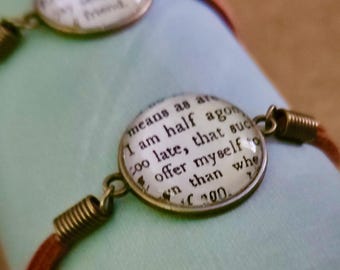 May include: Three brown leather bracelets with circular, antique-style charms. Each charm features text from a book, with a bronze-colored metal frame and spring-like connectors. The bracelets are displayed on a light blue surface.