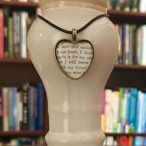 May include: A heart-shaped pendant necklace with a black cord. The pendant is made of glass and features a vintage book page with the text "I love thee agains your heart, I think spite it for my sak or I will never ich my friend too wise t".