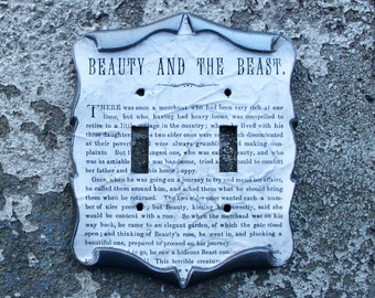 May include: A decorative light switch cover with the title "BEAUTY AND THE BEAST" printed at the top. The cover has a scroll-like design and features text from the story. It has two switch openings and a distressed, vintage appearance.