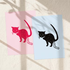 Könnte beinhalten: Zwei Kunstdrucke mit Katzenillustrationen. Einer zeigt eine rote Katze auf rosa Hintergrund, der andere eine schwarze Katze auf hellblauem Hintergrund. Jede Katze hat eine Sprechblase mit "CAT CALLING".