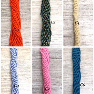 May include: Six strands of seed beads in various colours, including orange, green, cream, light blue, pink, and teal. The beads are arranged vertically in a row, with each strand labelled with a number.