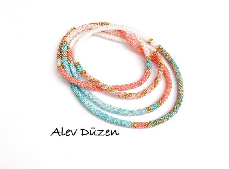 May include: A multi-strand beaded necklace with a white, peach, and turquoise color scheme. The necklace is made of small beads and has a subtle gold accent.