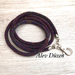 May include: A dark purple beaded lanyard with a silver clasp. The beads have a subtle iridescent sheen.