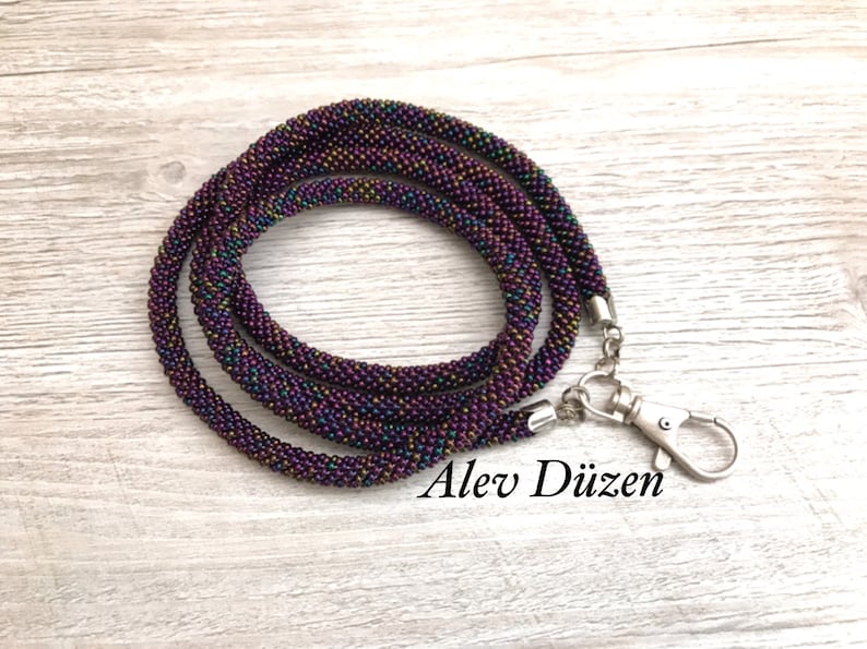 May include: A dark purple beaded lanyard with a silver clasp. The beads have a subtle iridescent sheen.