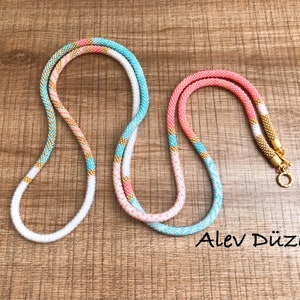 May include: Two beaded necklaces, one turquoise and white with gold accents, and one pink and white with gold accents, on a wooden surface. The necklaces are both about 40 inches long and have a gold clasp.