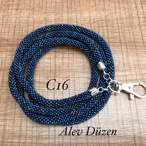 May include: A dark blue and iridescent beaded lanyard with a silver clasp and a silver chain. The lanyard is coiled and the text "Ci6" is visible in the centre of the image.