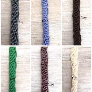 May include: Six strands of seed beads in different colours, including grey, blue, brown, green, purple, and white. The beads are arranged in rows and labelled with numbers C25 through C30.