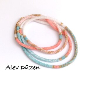 May include: A multi-strand beaded necklace with white, pink, and turquoise beads. The necklace is made of small, round beads and has a gold accent.