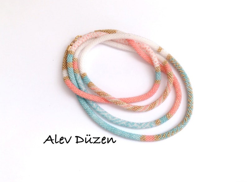 May include: A multi-strand beaded necklace with white, pink, and turquoise beads. The necklace is made of small, round beads and has a gold accent.