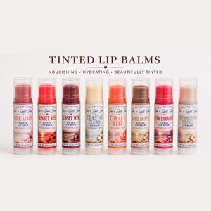 May include: A selection of tinted lip balms in clear tubes, each with a different name such as "Pink Sands" and "Sunset Kiss." The balms are displayed in a line, showing off a range of colours and textures, with the words "Tinted Lip Balms" at the top.