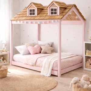 May include: A pink wooden bed frame shaped like a house with a shingled roof and two small windows. The bed is made up with pink bedding and decorative pillows. A round woven rug sits on the floor.