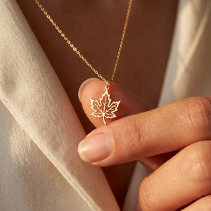 May include: A gold-toned necklace featuring a delicate, open-work maple leaf pendant suspended from a thin, matching chain. The pendant displays a detailed, cut-out vein structure throughout the leaf shape, creating a lightweight and intricate appearance.