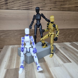 May include: Three articulated action figures in black, gold, and white with purple accents. The figures are posed on a gray platform and a wooden surface. The figures are designed to be posed in various positions.