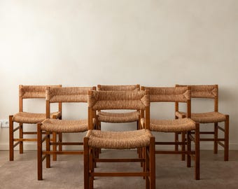 May include: A set of five wooden chairs arranged in a group. Each chair features a warm brown wooden frame with a woven rush seat and a matching woven rush backrest. The chairs have straight legs and a simple, functional construction.