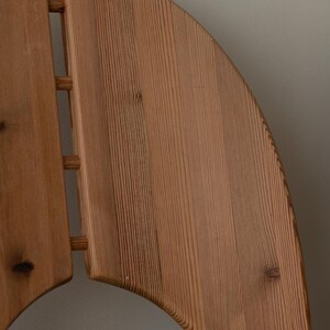 Puede incluir: Primer plano del respaldo de una silla de madera. El respaldo de la silla est&aacute; hecho de madera de color claro con vetas visibles. El dise&ntilde;o incluye una parte superior curva y listones verticales, mostrando una est&eacute;tica minimalista. La madera tiene nudos y variaciones naturales.