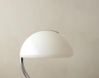 May include: A table lamp featuring a large, white, dome-shaped shade supported by a curved, polished chrome arm. The lamp has a circular chrome base and a smooth, reflective finish on the metal components, creating a clean and functional lighting fixture.