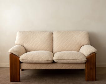 May include: A two-seater sofa featuring cream-colored fabric with a subtle diagonal textured pattern. The piece is supported by thick, solid wooden armrests and legs in a medium-brown tone, with two plush seat cushions and two back cushions.