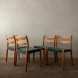 Puede incluir: Cuatro sillas de madera con acabado marrón claro. Las sillas tienen un respaldo curvo con tres listones horizontales y un asiento verde oscuro. Las patas son rectas y cilíndricas.