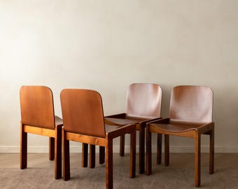 May include: A set of four wooden chairs with a medium brown finish. Each chair features a curved backrest and a flat seat supported by four straight legs. The chairs are arranged in a group, showing a consistent design with smooth surfaces.