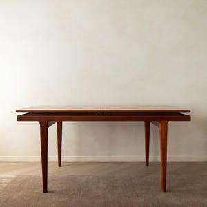 Puede incluir: Una mesa de comedor rectangular de madera con un acabado marrón cálido. La mesa presenta una superficie superior plana con una costura visible en el centro, apoyada por cuatro patas cónicas que se extienden desde las esquinas del marco.