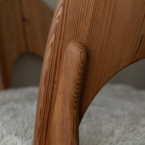 Puede incluir: Una silla de madera con un marco curvo de color marr&oacute;n claro con vetas visibles y un coj&iacute;n de asiento blanco texturizado. La estructura muestra uniones suaves y redondeadas que conectan el respaldo con las patas.