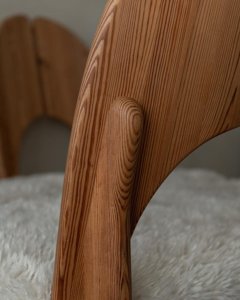 Puede incluir: Una silla de madera con un marco curvo de color marr&oacute;n claro con vetas visibles y un coj&iacute;n de asiento blanco texturizado. La estructura muestra uniones suaves y redondeadas que conectan el respaldo con las patas.