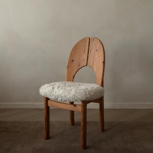 Puede incluir: Una silla de madera con un acabado de veta natural en color marr&oacute;n claro y un respaldo arqueado en dos piezas. El asiento est&aacute; cubierto con un coj&iacute;n grueso de piel sint&eacute;tica blanca de pelo largo, sostenido por cuatro patas rectas.