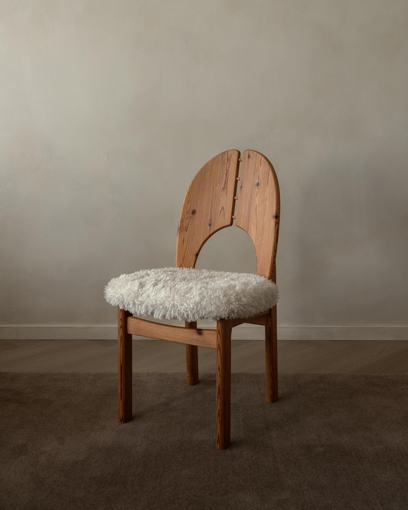Puede incluir: Una silla de madera con un acabado de veta natural en color marr&oacute;n claro y un respaldo arqueado en dos piezas. El asiento est&aacute; cubierto con un coj&iacute;n grueso de piel sint&eacute;tica blanca de pelo largo, sostenido por cuatro patas rectas.