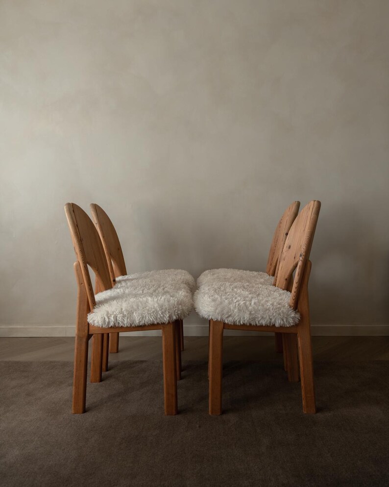 Puede incluir: Un conjunto de cuatro sillas de madera con marcos de color marr&oacute;n claro y respaldos curvos. Cada silla cuenta con un coj&iacute;n de asiento grueso de piel sint&eacute;tica blanca y peluda. Las sillas est&aacute;n dispuestas en dos pares frente a frente.