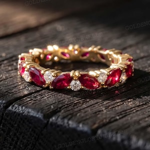 May include: A gold eternity band featuring an alternating pattern of marquise-cut red rubies and round-cut white diamonds. The ring is crafted with a polished metal finish, showcasing a continuous arrangement of gemstones around the entire band.