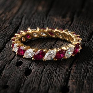 Peut inclure: Une bague alliance en or jaune, ornée d'une alternance de rubis rouges et de diamants blancs transparents, tous deux taillés en marquise, disposés en un motif circulaire continu tout autour de la circonférence de l'anneau en métal.