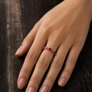 May include: A gold ring featuring a series of alternating marquise-cut and round-cut red rubies set along the band. The gemstones are arranged in a repeating pattern, showcasing a vibrant crimson hue against the polished gold metal setting.