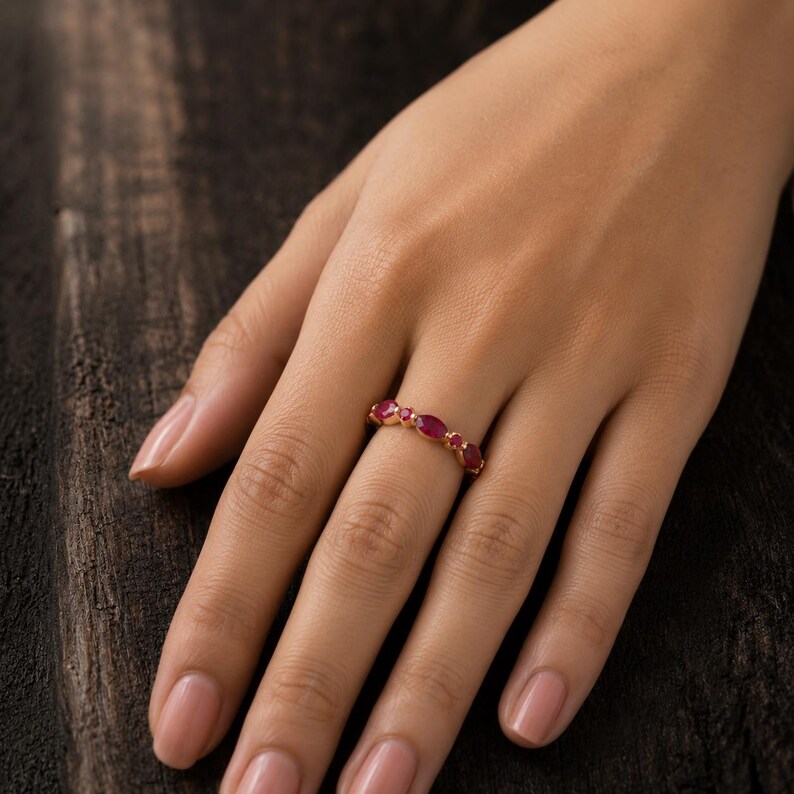 May include: A gold ring featuring a series of alternating marquise-cut and round-cut red rubies set along the band. The gemstones are arranged in a repeating pattern, showcasing a vibrant crimson hue against the polished gold metal setting.