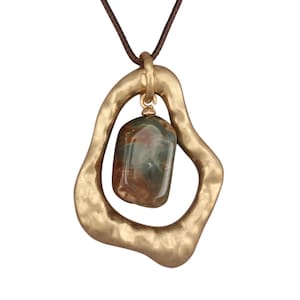 Puede incluir: Un collar con colgante que presenta un marco de metal dorado martillado de forma irregular suspendido de un cordón marrón. Una piedra rectangular lisa y pulida con patrones de remolinos en verde, marrón y crema está unida al centro del marco.