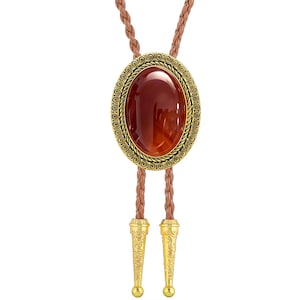 Peut inclure: Une cravate bolo avec une pierre ovale brun-rouge dans un cadre filigrané doré. Le cordon marron tressé mène à des embouts décoratifs dorés. Un accessoire de style western classique.