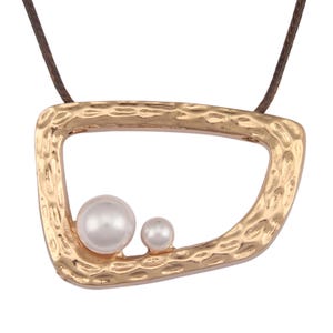 May include: A gold-toned pendant with an irregular, hammered texture frame featuring two white spherical pearls of different sizes attached to the bottom edge, suspended from a thin brown cord necklace.
