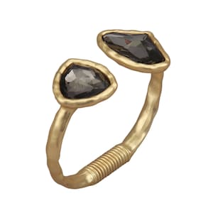 Könnte beinhalten: Ein goldfarbenes Armreif-Armband mit zwei unregelmäßig geformten, dunkelgrauen Edelsteinen. Das Armband hat eine strukturierte, gehämmert Oberfläche und ein gewickeltes Detail in der Nähe der Mitte. Die Edelsteine sind in einer goldenen Lünette gefasst.