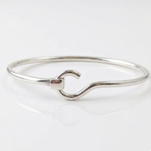 Peut inclure: Un bracelet jonc argenté avec un fermoir crochet. Le bracelet a une finition lisse et polie et un design simple et élégant. Le fermoir crochet est rectangulaire.