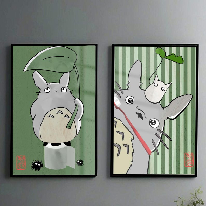 May include: Two framed art prints featuring the animated character Totoro. The left print shows Totoro holding a leaf umbrella against a green background. The right print depicts Totoro with a small white creature on its head, set against a striped green background.