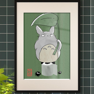 May include: Framed art print depicting a cartoon Totoro character with a leaf umbrella. The gray Totoro is sat on a roll of toilet paper against a green backdrop. Two small black soot sprites are also present. The print is in a black frame.