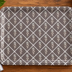 May include: A rectangular serving tray featuring a dark gray background with a white diamond grid pattern. Each diamond contains a single white line-art flower with a stem and leaves. The tray has rounded corners and a smooth, glossy finish.