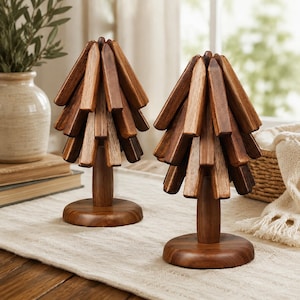 May include: Two decorative tabletop sculptures shaped like stylized trees, each crafted from multiple pieces of dark brown wood. The trees feature a central cylindrical trunk mounted on a circular base, with angled wooden slats forming the foliage.