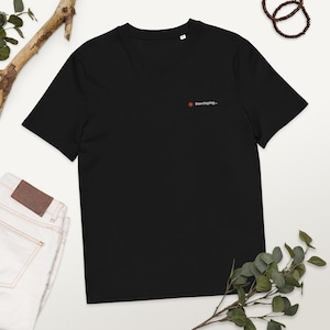 Op de afbeelding: Zwart T-shirt met het woord "Developing..." in oranje en witte tekst. Het shirt heeft een ronde hals en is gemaakt van een zacht materiaal. Het T-shirt wordt gepresenteerd op een witte ondergrond.