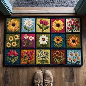 May include: A rectangular doormat with a grid pattern of embroidered flowers. Each square displays a different flower, such as sunflowers and daisies, in vibrant colours. The mat has a dark blue border. The mat is on a wooden floor.