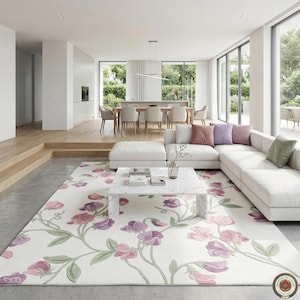 Könnte beinhalten: Ein modernes Wohnzimmer mit einem großen weißen Ecksofa, einem Marmor-Couchtisch und einem floralen Teppich. Der Teppich zeigt ein Muster aus rosa und lila Blumen mit grünen Stielen. Große Fenster bieten einen Blick ins Freie.